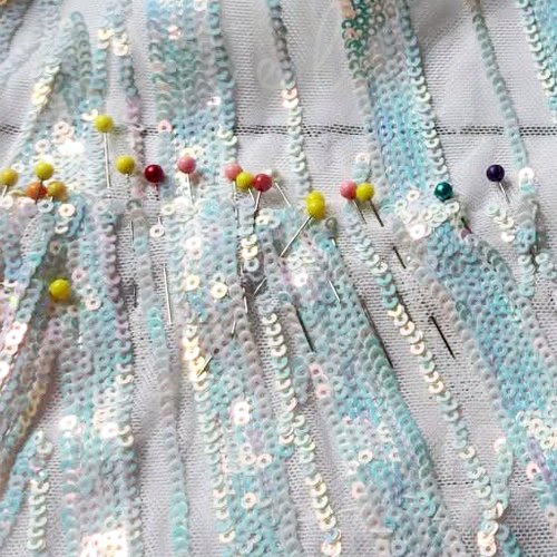 Sequined fabric pinned with colored marking pins to match the pattern by hand