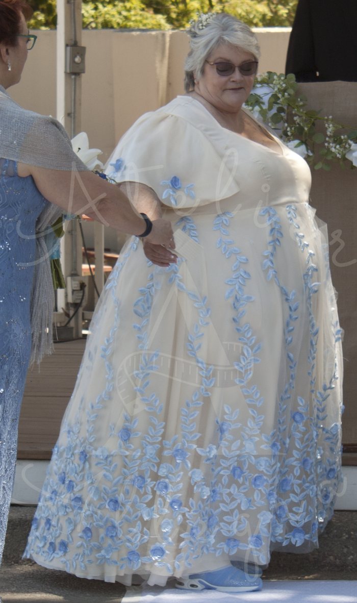 Bride in profile wearing an ivory A-line gown with pale blue floral vine appliqué and embroidery, being escorted down the aisle