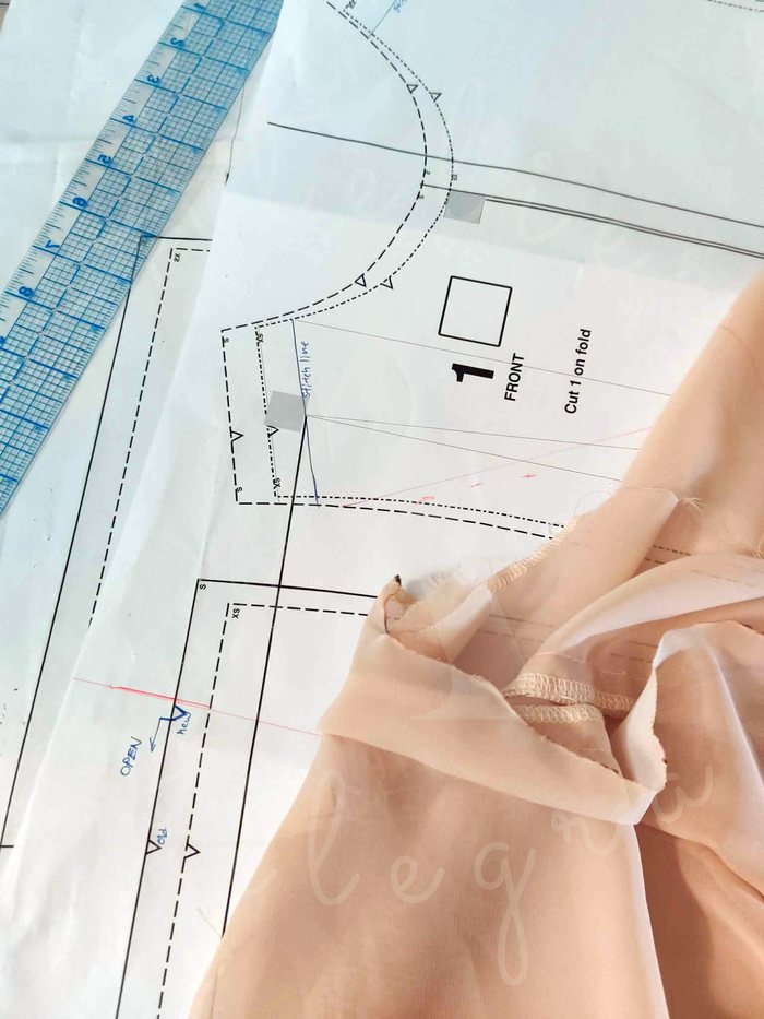 Hand-marked paper pattern piece with shoulder fit alterations, alongside pinned fabric